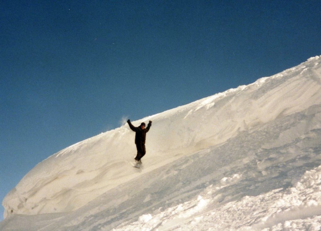 A snowboarder carving at speed down a snow-covered mountain slope